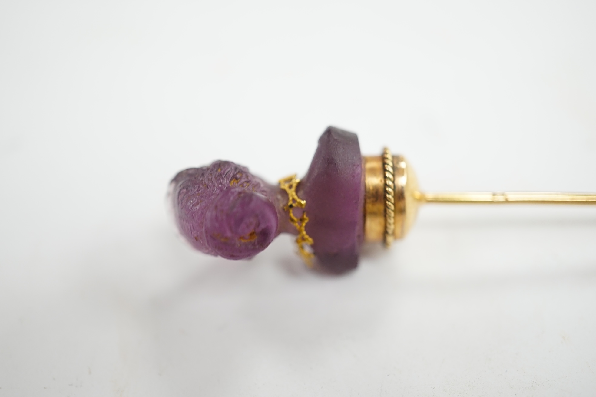 An early 20th century French yellow metal (18ct poincon mark) and amethyst paste set stick pin, the terminal modelled as the bust of a lady, 96mm, gross weight 5.6 grams. Condition - poor to fair